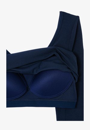 Dunkelblaues, geripptes Stoffkleidungsstück, das teilweise gefaltet ist, um einen passenden gepolsterten BH mit geformten Cups und breiten Trägern darunter zu zeigen.