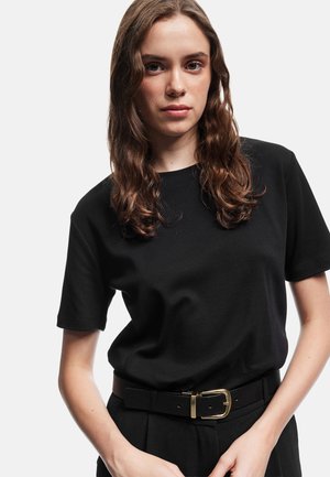 Zwarte katoenen t-shirt met ronde hals en korte mouwen, gecombineerd met high-waisted broek met een zwarte riem en gouden gespdetail.