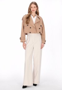 Avklippt beige trenchcoat med dubbelknäppning, dekorerade detaljer och uppvikta ärmar, kombinerad med cremefärgade vida byxor med hög midja.