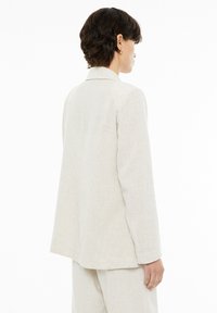Light beige linen blazer with a tailored fit, notched lapels, and long sleeves. Features a smooth texture and a vented back for airflow.