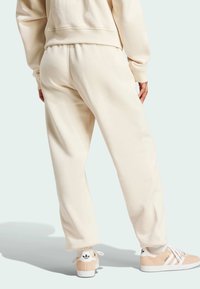 Crèmefärgade träningsoverallsbyxor med elastiskt midjeband, avslappnad passform och sidoseams detaljer; tillsammans med beige och vita sneakers med en logotyp.