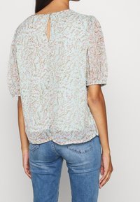 Jasnoniebieska bluzka z kwiatowym wzorem w odcieniach różu i brązu, z krótkimi puffowanymi rękawami, zapięciem w kształcie dziurki z tyłu oraz miękkim, zwiewnym materiałem.