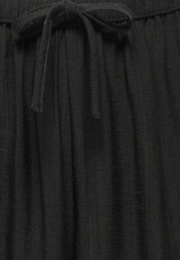 Gros plan d'un pantalon en tissu noir texturé avec une ceinture élastique et un cordon noué à l'avant au centre.