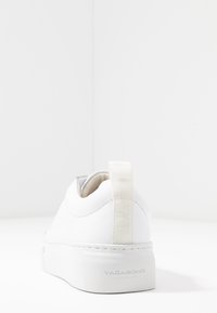 Hvit sneaker med avrundet design, glatt lær overtopp, polstret krage og en kontrasterende kremfarget pull-tab. Har en teksturert såle.