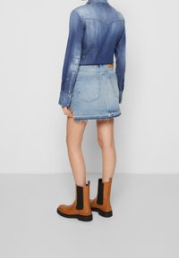 Džínová košile s modrým gradientem, dlouhé rukávy. Doplněná o džínsovou sukni s roztrhaným lemem a hnědé kotníkové boty s černými elastickými panely.