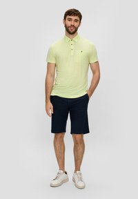 Jasnożółta koszulka polo z krótkim rękawem, z kołnierzykiem i kieszonką na piersi, zestawiona z granatowymi szortami i białymi trampkami. Swobodny krój, materiał z mieszanki bawełny.