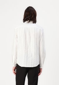 Witte langelijfshirt met verticale blauwe en beige strepen, met een relaxte pasvorm, knoopmanchetten en een geplooide achterkant voor extra textuur.