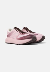 Se muestran dos zapatillas de correr elegantes, con un diseño en degradado rosa y cordones marrones oscuros, además de una suela gruesa y texturizada para mayor agarre.