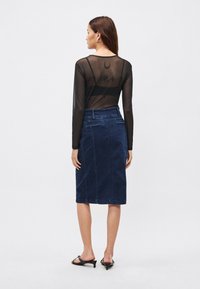 Juodas permatomas ilgomis rankovėmis viršus su nugaros piešiniu, derinamas su tamsiai mėlynu džinsiniu sijonu iki kelių, kuriame yra kišenėlės ir siūlės.