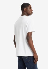 Weißes Baumwoll-T-Shirt mit kurzen Ärmeln und Rundhalsausschnitt. Schlichtes Design, lockere Passform, glatte Textur. Getragen mit blauen Jeans.