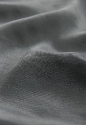 Detailní záběr na tmavě šedou texturu látky s jemnými záhyby a hladkým, těsně tkaným povrchem.