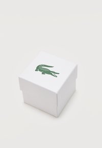 Λευκό τετράγωνο κουτί με ανάγλυφη υφή και πράσινο λογότυπο κροκοδείλου στο επάνω μέρος, φωτογραφημένο σε απλό λευκό φόντο.