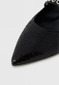 Μαύρο μυτερό παπούτσι καλυμμένο με μικρές γυαλιστερές παγιέτες, που δείχνει λεπτομερή υφή και μέρος της εσωτερικής επένδυσης.