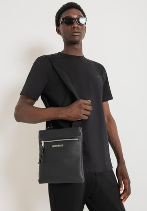 Borsa a spalla nera realizzata in materiale testurizzato, con tasca frontale con zip e tracolla. Marchio visibile sulla parte anteriore della borsa.