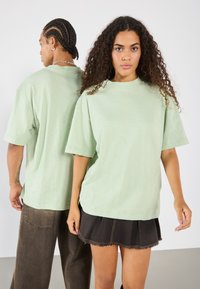 Světl zelené oversized tričko vyrobené z měkké tkaniny, s kulatým výstřihem a krátkými rukávy; nošeno s tmavými denimovými šortkami.
