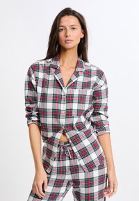Ensemble de pyjama en flanelle avec un motif à carreaux rouge, vert et blanc. La chemise a une fermeture à boutons et une poche sur la poitrine; le pantalon a une taille élastique.