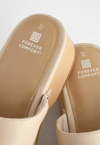 Bežīgas slaidās čības ar gludu ādas virsu un tekstūru gumijas zoli. Iezīmēts ar "Forever Comfort" logo baltā krāsā. Gaismas šuvju detaļa.
