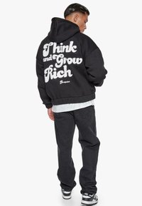 Sort hættetrøje med hvid tekst "Think and Grow Rich" på ryggen. Lavet af blødt stof, med en afslappet pasform, oversize design og kængurulomme.