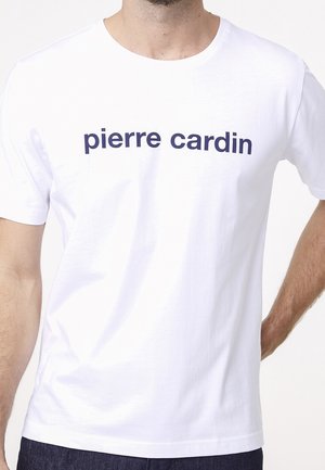 Mann trägt ein schlichtes weißes Kurzarm-T-Shirt mit "pierre cardin" in dunkelblauen Buchstaben über der Brust.