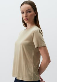 T-shirt beige a maniche corte con scollatura rotonda, texture liscia e cuciture laterali, progettato per una vestibilità comoda. Design semplice senza motivi.