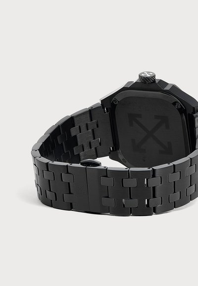 Montre-bracelet en métal noir avec bracelet lié, fond de boîtier carré avec un logo de flèche croisée, et une couronne texturée avec le même logo.