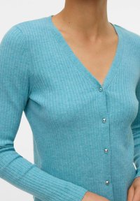 Cardigan bleu clair en tissu côtelé, avec un col en V, des manches longues et une fermeture à cinq boutons argentés à l'avant.
