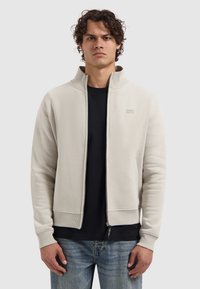 Light beige zip-up sweatshirt with high collar, ribbed cuffs, and hem; features a logo in a lighter shade on the left chest.