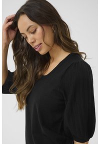 Schwarzer Pullover mit gerippten, puffartigen Ärmeln und rundem Ausschnitt, aus weichem Material mit glatter Textur hergestellt.