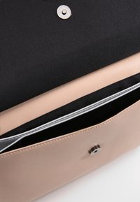 Svetle růžová kožená taška s černým interiérem, vybavená magnetickým uzávěrem a stříbrným zipem podél kapsy.