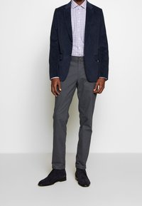 Blazer blu navy, camicia a quadri lilla chiaro, chino grigi e stivaletti alla caviglia in suede neri. Il blazer presenta due tasche frontali e rever a punta.
