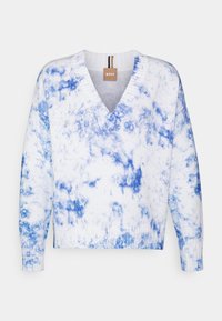 Vitt tröja med ett tie-dye-mönster i varierande blå nyanser, med v-halsdesign, ribbade muddar och nederkant. Varumärkesetikett synlig vid nacken.