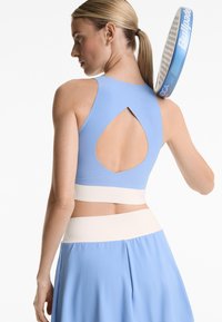 Light blue athletic crop top with a cut-out back design, paired with a matching skirt featuring a contrasting waistband. Paddle held behind.