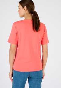 Koraalkleurig T-shirt met korte mouwen, gemaakt van zachte stof. Ronde halsontwerp, minimalistische stijl en een relaxte pasvorm. Achteraanzicht, gedragen met blauwe denim.