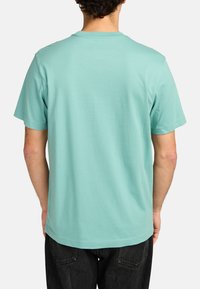 Camiseta de algodón verde menta con mangas cortas, escote redondo y un corte holgado. Parte trasera lisa sin logotipos ni patrones visibles.
