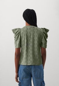 Top de color verde oliva con hombros abullonados, tejido texturizado con patrones en forma de ola, mangas cortas y un corte relajado.