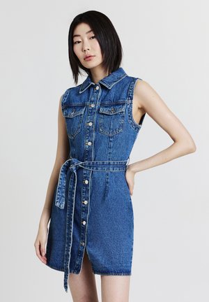 Robe en denim avec un col, sans manches, fermeture à boutons sur le devant et une ceinture en tissu à la taille. Couleur bleu clair avec deux poches poitrine.