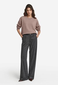 Ljust rosa oversized tröja med ribbad halsringning, ihop med höga, texturerade grå byxor. Sittande, spetsiga bruna klackar fulländar looken.