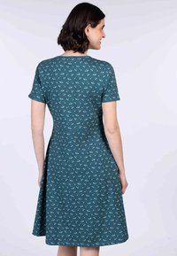 Ein tailliertes türkisfarbenes Kleid mit kurzen Ärmeln, das ein sich wiederholendes Blumenmuster in Hellblau und Creme zeigt. Ausgestellter Rockdesign.