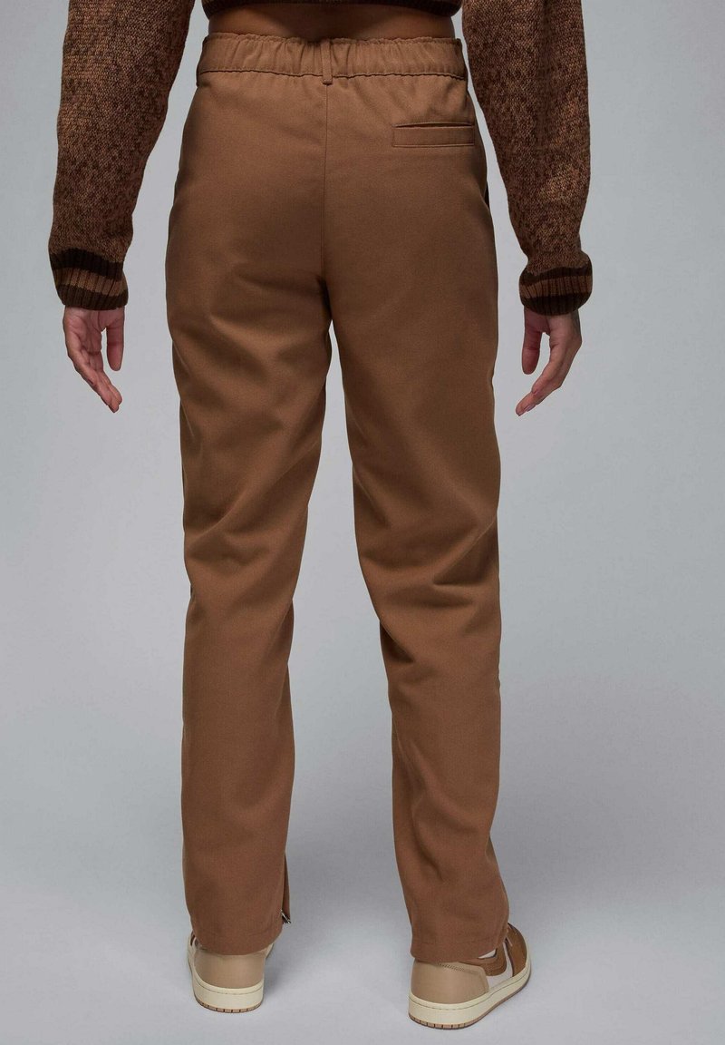 Pantaloni marroni con una vestibilità rilassata, cintura elastica e una tasca posteriore. Il materiale sembra liscio e resistente, con una leggera lucentezza.