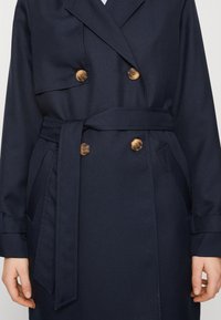 Abrigo de marinero de doble botonadura con cintura ceñida, confeccionado en tejido suave. Presenta grandes botones de bronce circulares y bolsillos laterales.