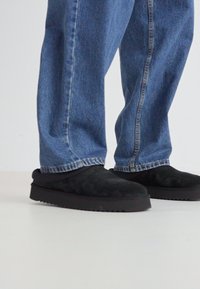 Zapatos de ante negros sin cordones con una suela de goma gruesa, combinados con unos vaqueros de denim azul deslavado con piernas rectas y costuras visibles.