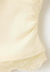 Gros plan sur un tissu couleur crème avec fronces latérales et délicate bordure en dentelle à l'ourlet.