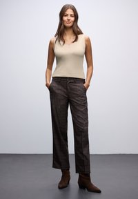 Top sin mangas beige combinado con pantalones de cuadros marrones, que cuentan con bolsillos y un cierre de botones. Persona que lleva botas cortas marrones.