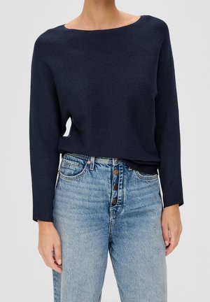 Granatowy sweter prążkowany z dekoltem w łódkę, długimi rękawami i luźnym krojem, zestawiony z jasnoniebieskimi dżinsami z wysokim stanem z zapięciem na guziki.