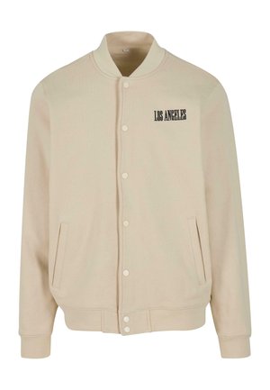 Beige bombázódzseki puha anyagból, patentos záródással, két oldalsó zsebbel és fekete hímzéssel a mellkasán, ami a "LOS ANGELES" feliratot tartalmazza.
