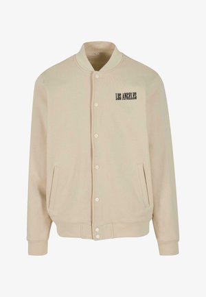 Beige bombázódzseki puha anyagból, patentos záródással, két oldalsó zsebbel és fekete hímzéssel a mellkasán, ami a "LOS ANGELES" feliratot tartalmazza.