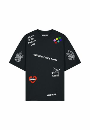 Uomo che indossa una t-shirt nera oversize con testo bianco e rosso, dadi fiammeggianti sulle maniche, patch colorati smiley e a forma di cuore sul petto.