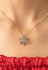Gold chain necklace featuring a snowflake pendant adorned with clear gemstones and intricate detailing, resting on a textured neckline.