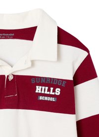 Gestreiftes Poloshirt aus roter und weißer Baumwolle. Verfügt über einen Kragen, eine Knopfverschluss und einen Aufdruck mit "SUNRIDGE HILLS SCHOOL" in marineblauer und weißer Schrift.