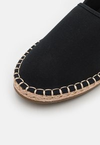 Espadrille en toile noire avec un bout rond, bord en jute cousu et une semelle en caoutchouc plate. Design simple avec une surface supérieure texturée.